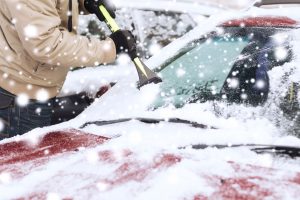 Scraping ice off snowy windshield.