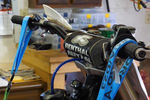 Secure handlebars to true a dirt bike rim without a stand.