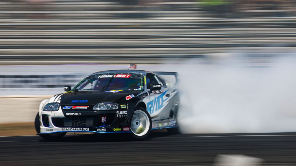 Rad Dan drifts around a corner with smoke in the background and an AMSOIL logo in view.